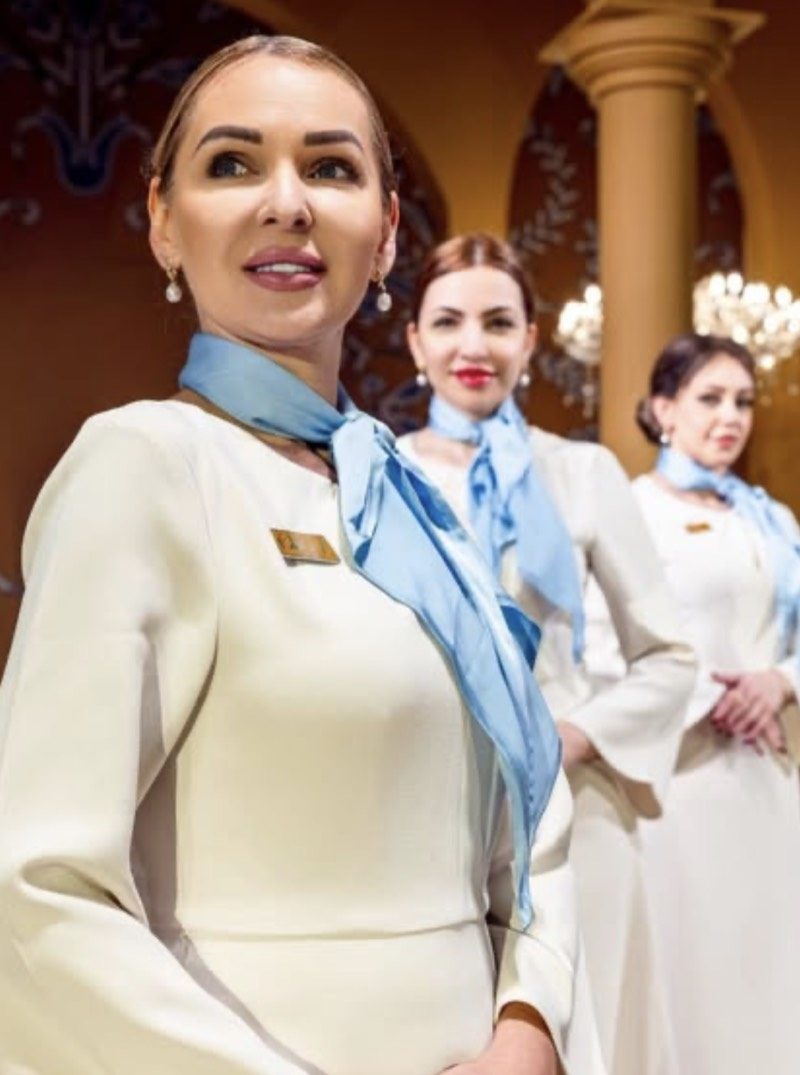 Three Voil&agrave; Protocol hostesses in ivory uniform and blue scarves in the venue hall