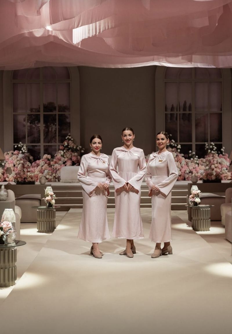 Three Voil&agrave; Protocol hostesses in blush, in a hall banked with roses