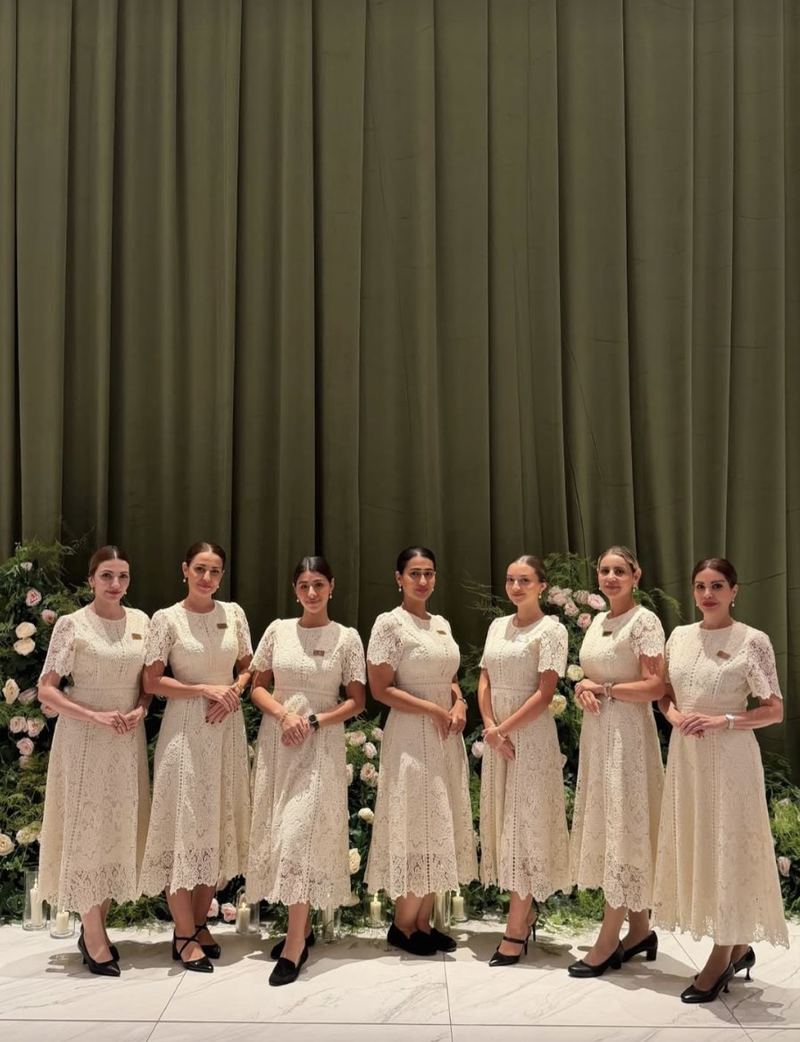 Seven Voil&agrave; Protocol hostesses in ivory lace before olive drapes and white roses
