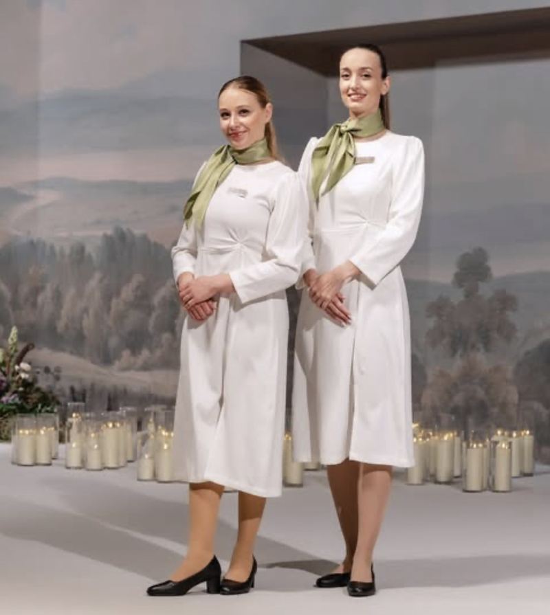 Two Voil&agrave; Protocol hostesses in sage scarves before a painted mural and candles