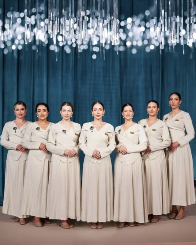 Seven Voil&agrave; Protocol hostesses lined up against teal velvet