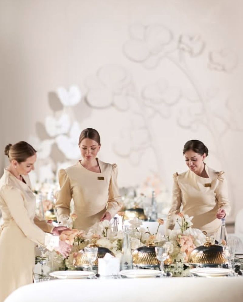 Three Voil&agrave; Protocol hostesses dressing a guest table before a moulded wall
